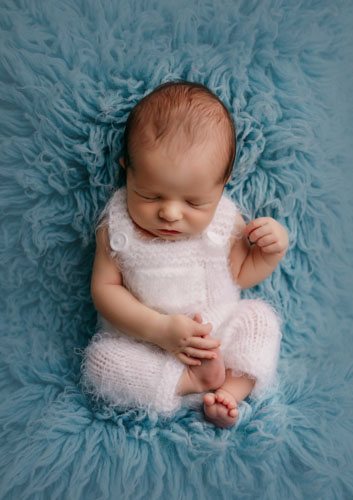 Newborn baby in white outfit and blue background photographed in Preston photography studio