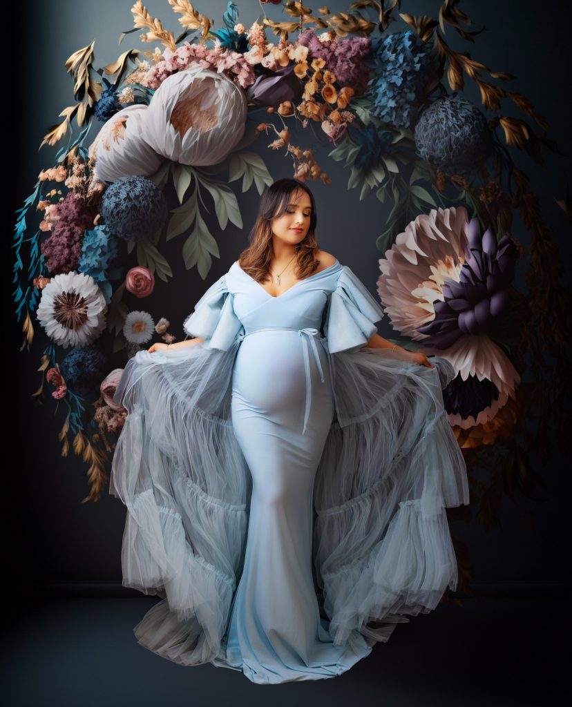 Pregnant woman in a flowing blue dress posing against a flowery background during a maternity photoshoot in Preston, Lancashire.